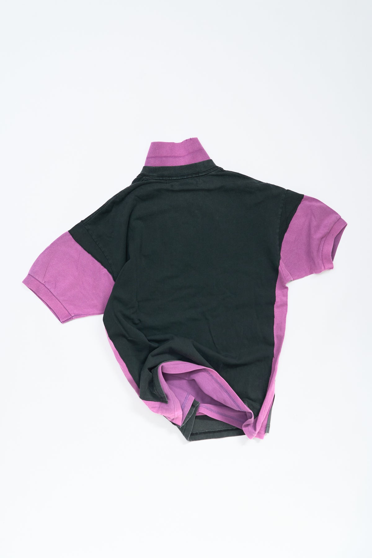 A short-sleeve polo shirt shown from the back, featuring a faded black body with contrasting pink collar, sleeve cuffs, and side trim, laid flat on a white background.